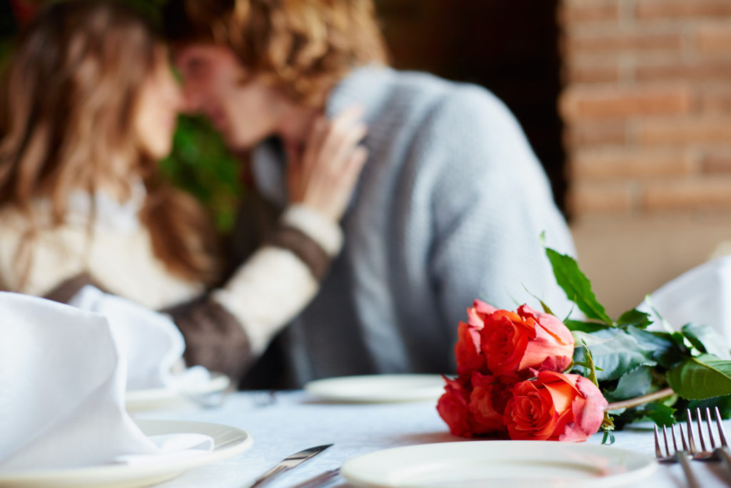 A bunch of red roses on served table and young lovers on background